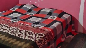 Une chambre aux murs roses, un lit recouvert d’une couvre-lit à motifs, un appareil de climatisation et une fresque murale représentant un arbre.