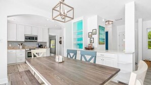 A modern kitchen with white cabinetry, a wooden dining table, and a built-in island with seating. - Splash & Explore (St. Augustine)