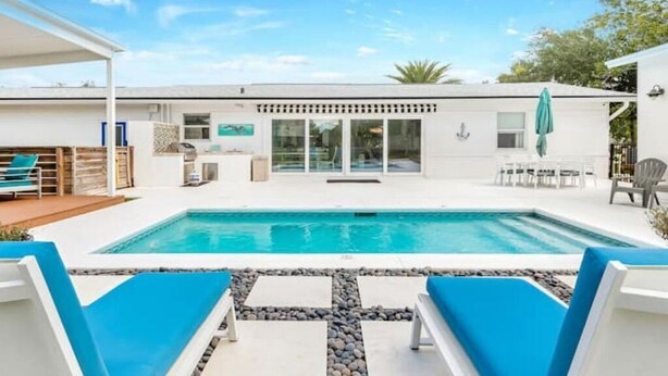 A modern pool area with a clear blue pool, surrounded by white lounge chairs and a stone pathway. - Splash & Explore (St. Augustine)