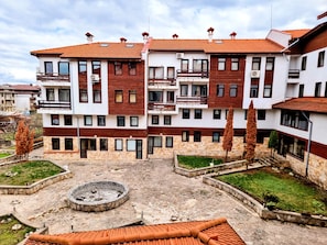 A multi-story residential building with balconies, a courtyard with a circular stone feature, and a mix of brick and stone facade.