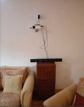 A room with a flat-screen TV mounted on a wooden cabinet, a beige sofa, and a patterned throw pillow. - Mountain Paradise 1 - 1 Bedroom South Facing Balcony - 300mbps Wi-fi (Bansko)