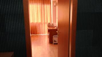 Ein Hotelzimmer mit Holzboden, Holztür und Blick auf einen Raum mit Bett und Vorhängen.