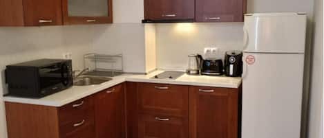 A compact kitchen with wooden cabinets, a white refrigerator, a microwave, and a coffee maker.