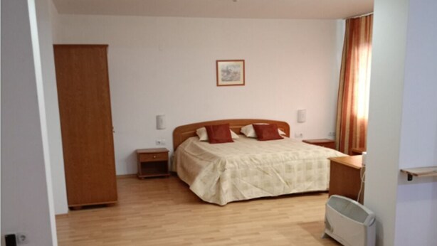 A bedroom with a wooden floor, a bed with a beige cover, a nightstand, a radiator, and a wooden wardrobe. - Mountain Paradise 1 - 1 Bedroom South Facing Balcony - 300mbps Wi-fi (Bansko)