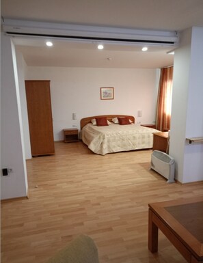 A bedroom with a wooden floor, a bed with a beige cover, a nightstand, a radiator, and a wooden wardrobe. - Mountain Paradise 1 - 1 Bedroom South Facing Balcony - 300mbps Wi-fi (Bansko)