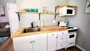 Una cocina compacta con encimera de madera, armarios blancos, un lavabo de acero inoxidable, una estufa y un microondas.