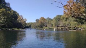 Un río flanqueado por árboles, un puente a lo lejos y cielo despejado.