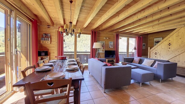 Interior d'una cabana de fusta amb menjador, sofà i televisió.