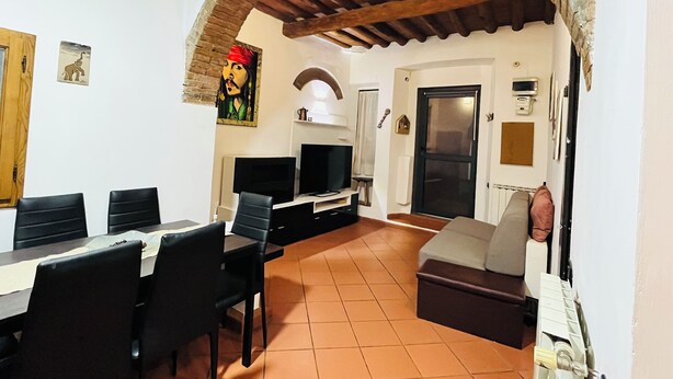 Una sala de estar con televisor, sofá y comedor con sillas.