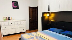 Un dormitorio con cama, cómoda, puerta y lámpara fijada a la pared.