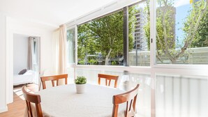 Ein modernes Zimmer mit einem runden Tisch, Holzstühlen, einer Topfpflanze und großen Fenstern mit Blick auf Bäume und Gebäude.