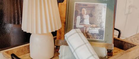 Una bandeja de madera con una lámpara blanca, un libro titulado 'Magnolia Table' y una toalla blanca doblada.