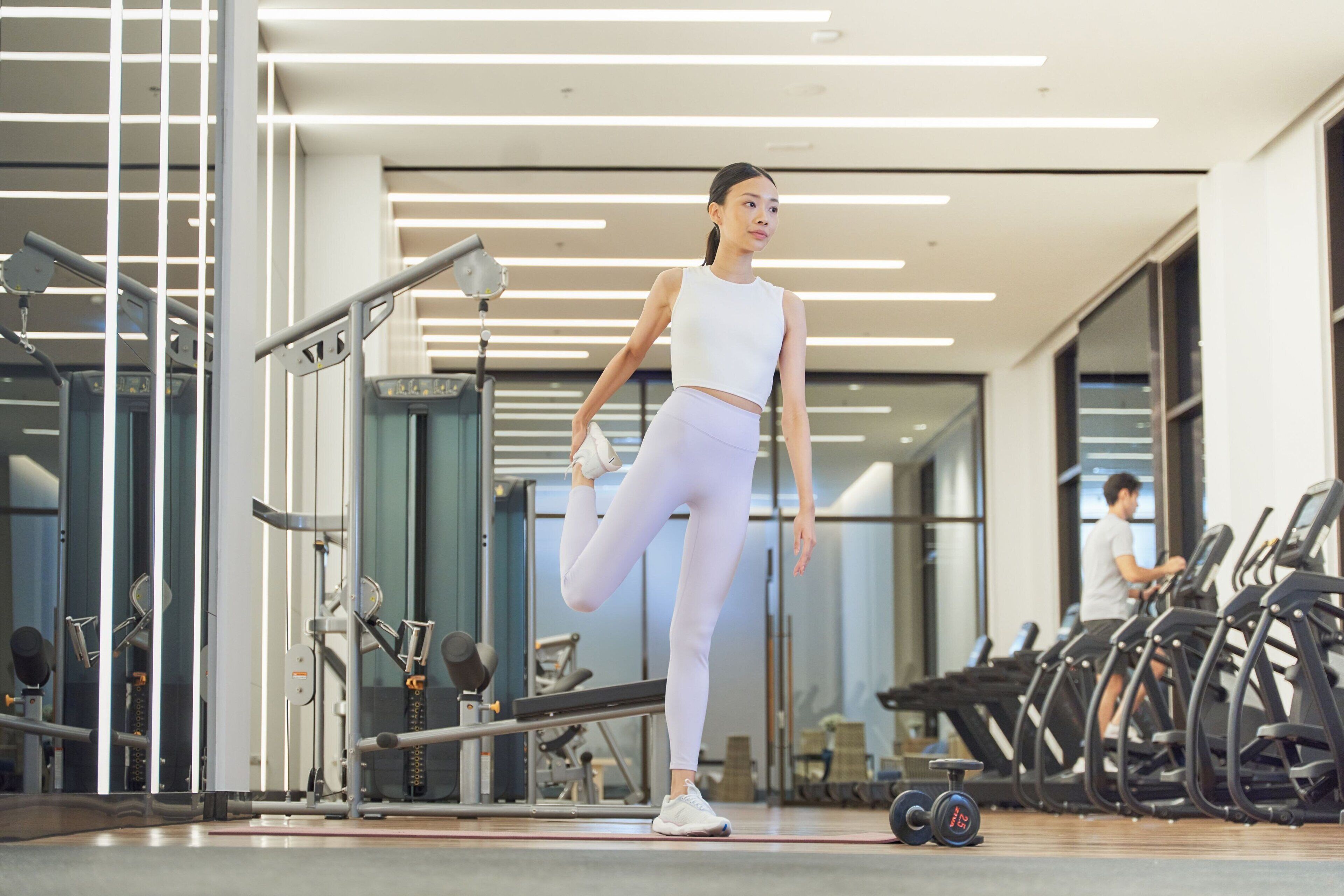 A gym with exercise equipment, a person stretching, and treadmills in the background.
