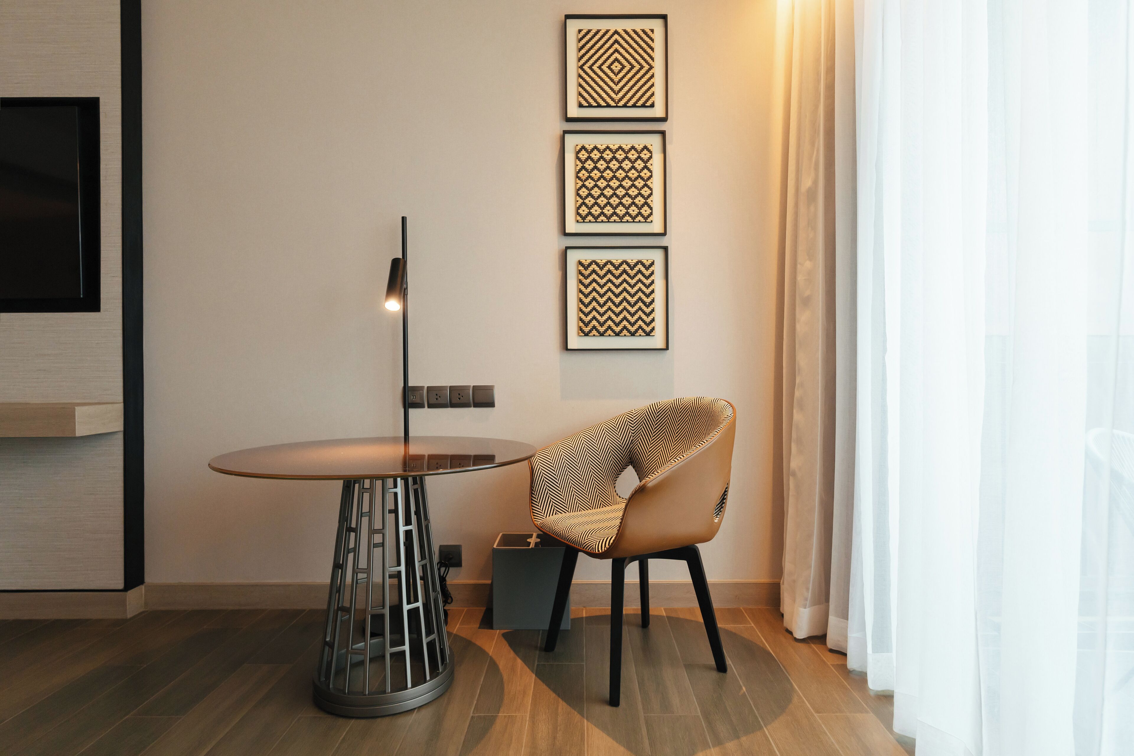 A modern room with a round glass table, a patterned chair, and three framed wall art pieces.