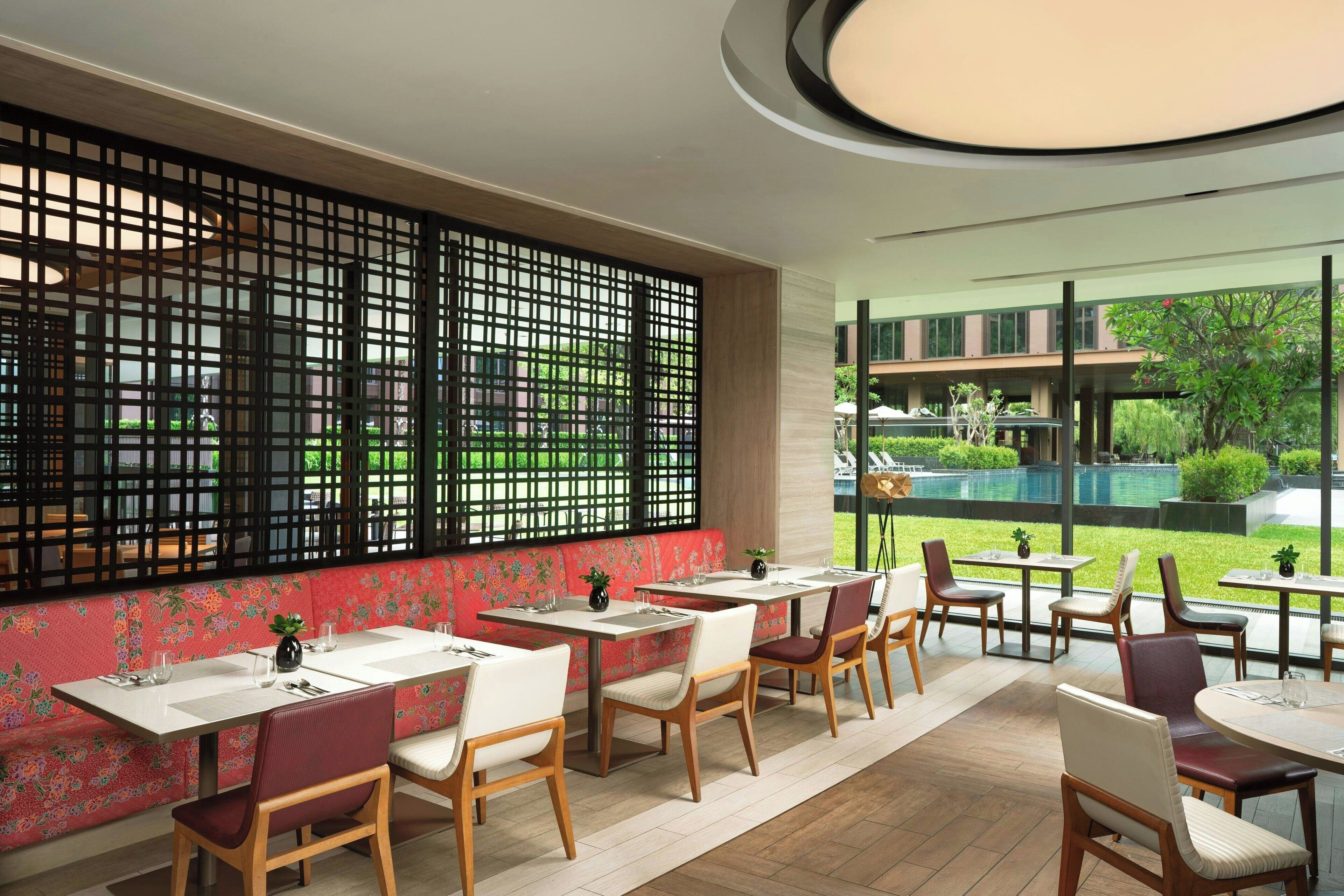 A restaurant with a long counter, cushioned seating, and a view of a swimming pool.