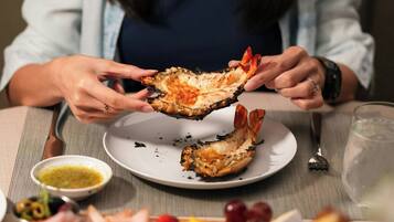 A person holding a cooked lobster shell, a plate with remnants of food, a small bowl of sauce, and a glass of water on a table.