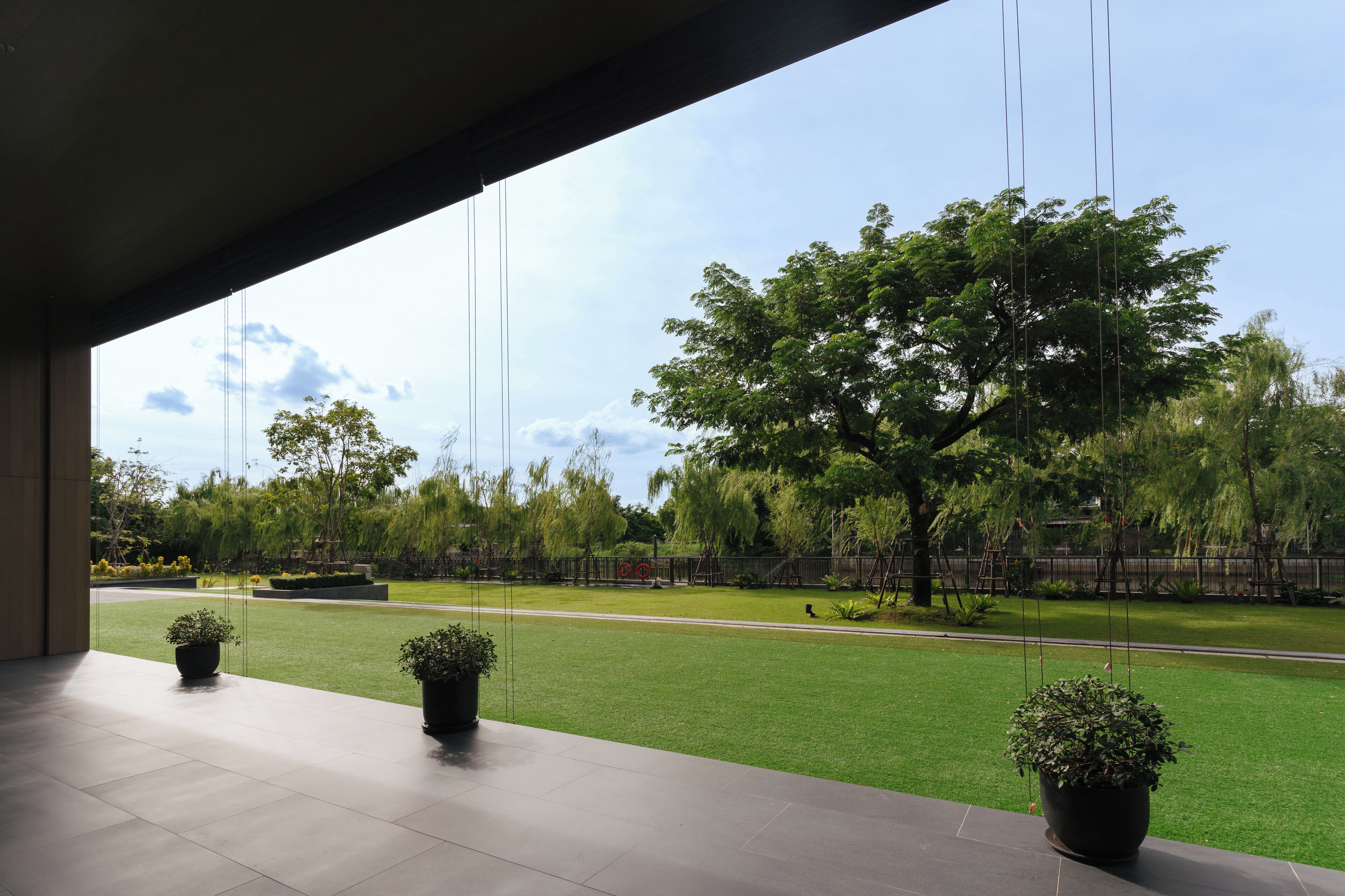 A modern building with a covered outdoor area featuring potted plants and a view of a well-maintained lawn and trees.