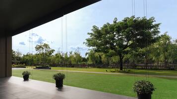 A modern building with a covered outdoor area featuring potted plants and a view of a well-maintained lawn and trees.