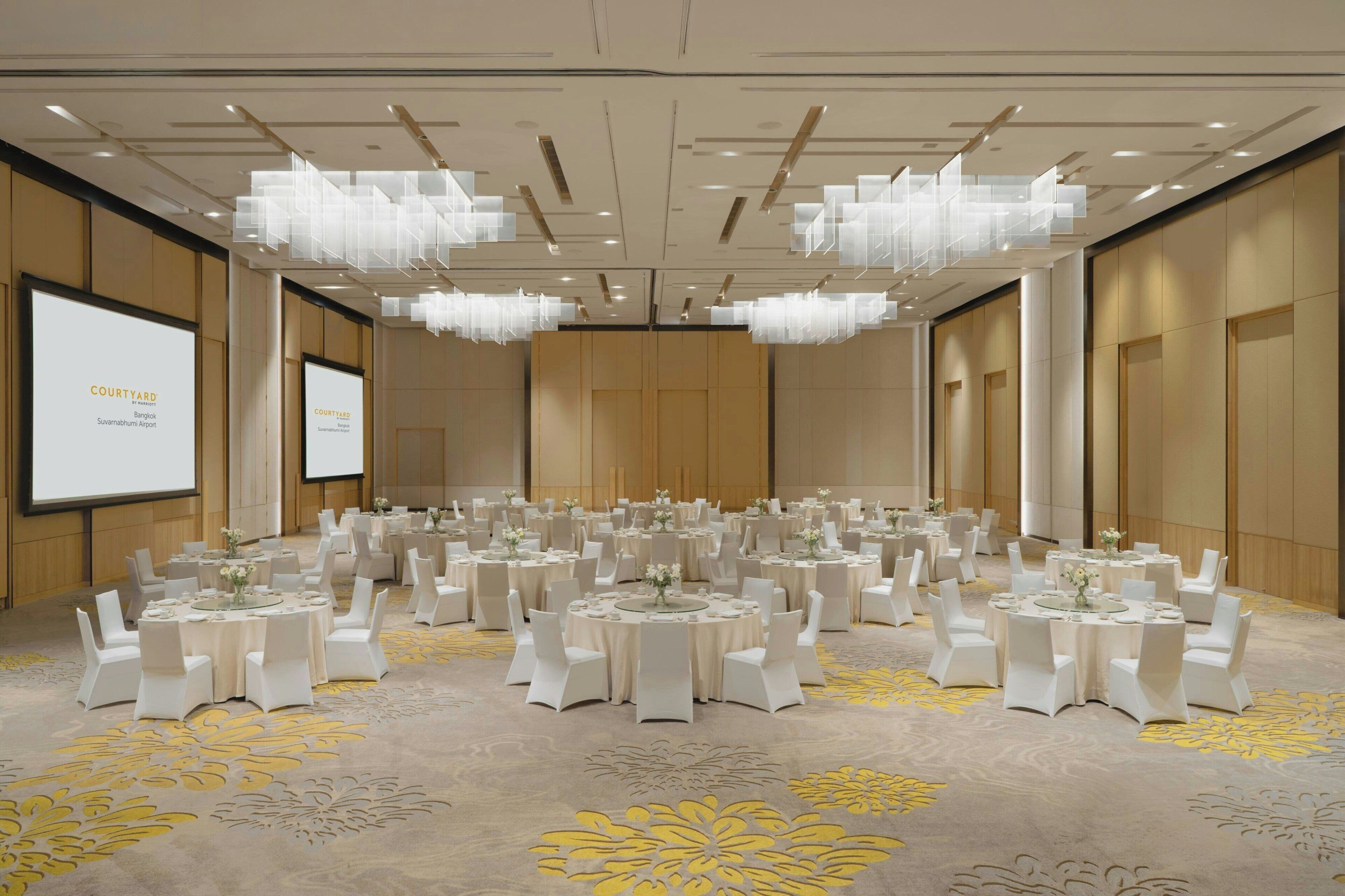 A large conference room with multiple round tables, white chairs, and chandeliers.