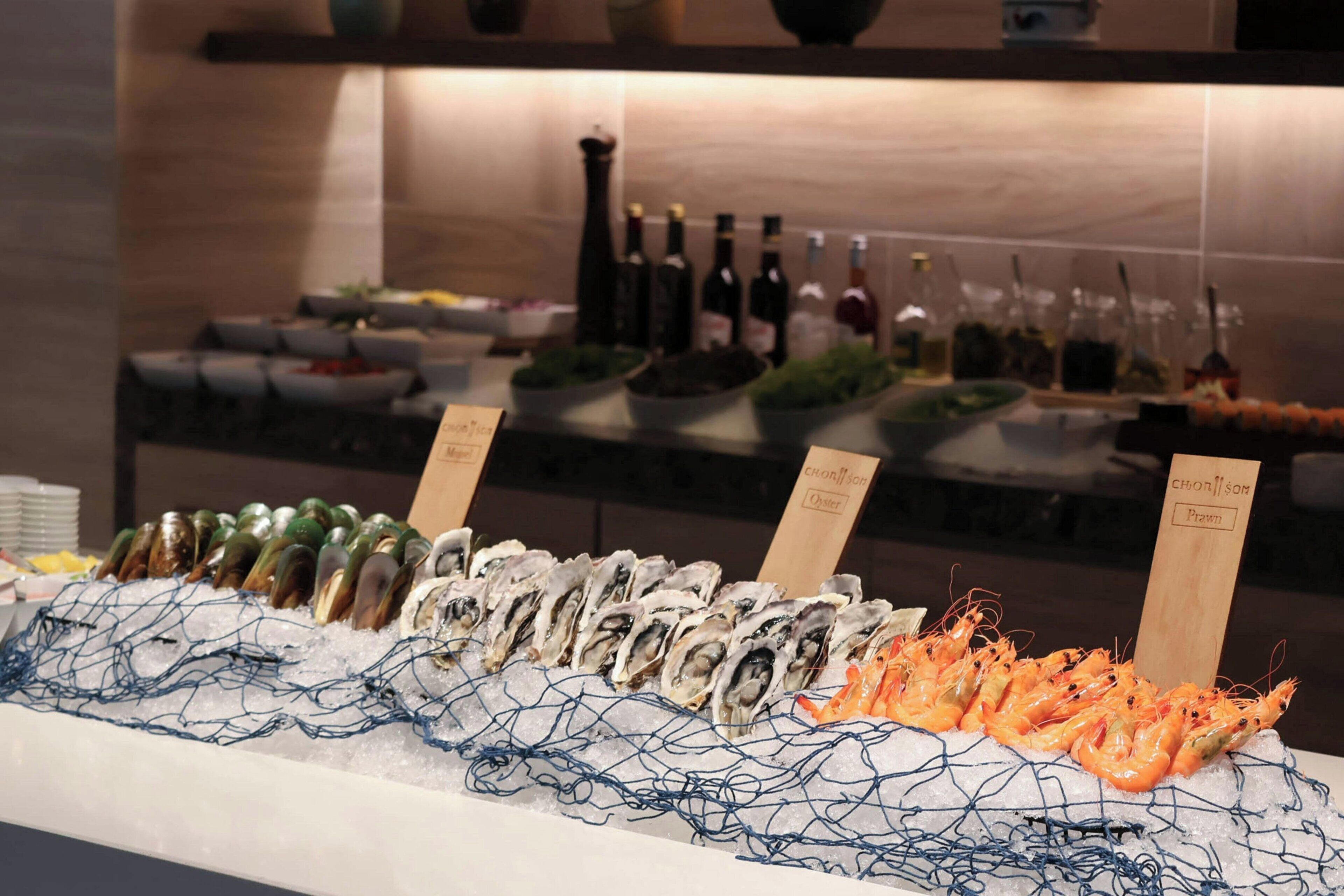 Een visdisplay met oesters, mosselen en garnalen, op ijs gepresenteerd, met labels die de soorten aangeven.