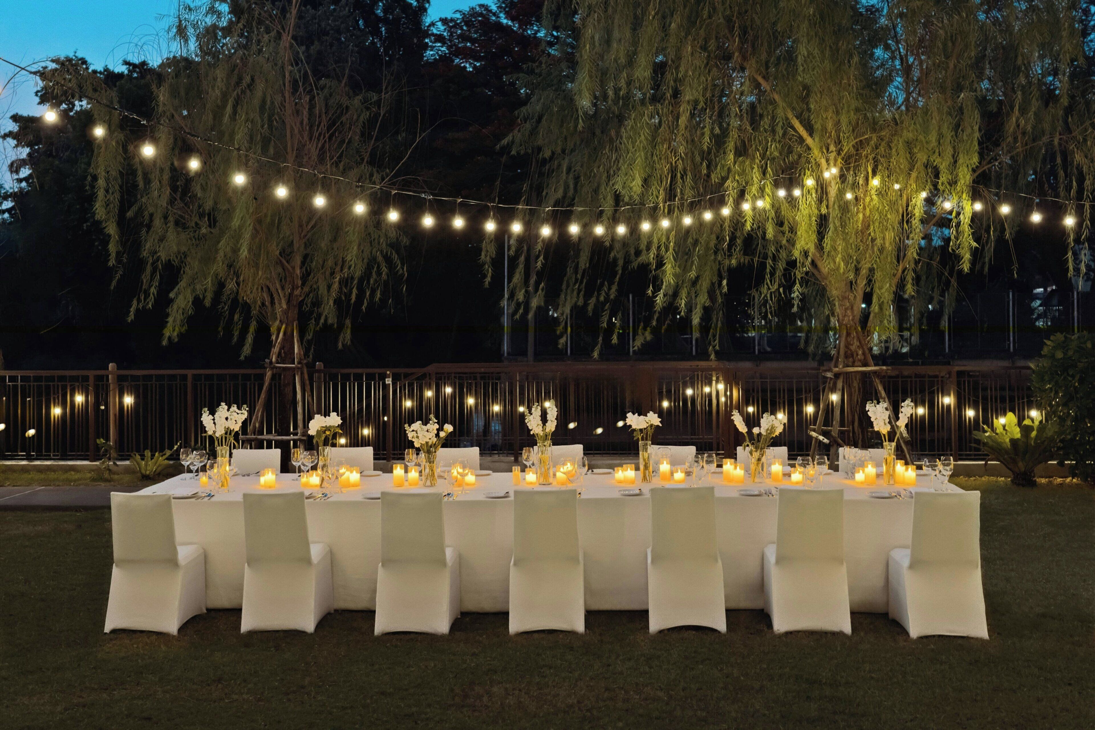An outdoor dining area with string lights, white tablecloths, and candles.
