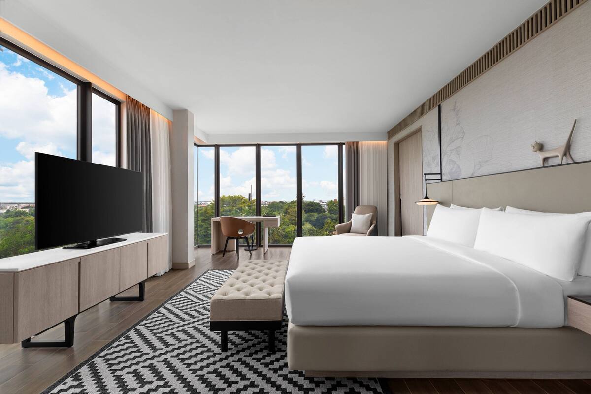 Ett modernt hotellrum med en stor säng, en platt-TV, ett skrivbord och utsikt över staden.