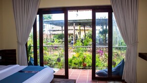 A room with a bed, a wooden bench, and a view of a garden through a glass door. - Kampot Eco Village (Kampot)