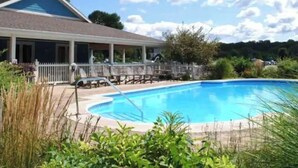 A pool area with a covered seating area and a building with a sloped roof. - SoHappy Haven - 6 bdrm, Game Room, Year Round Pools, Hot Tub, Marina & Clubhouse (South Haven)