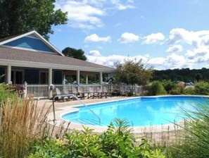 Relax by the pool surrounded by lush greenery and trees, with a covered patio area and lounge chairs nearby.