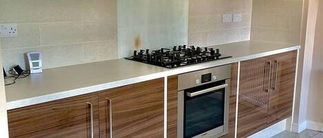 Une cuisine moderne équipée d’une cuisinière à gaz, d’un four et de meubles de rangement en bois.