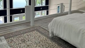 Une chambre avec un grand lit, une vue sur les arbres par les fenêtres et un ventilateur de plafond.