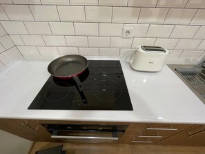 Une cuisine dotée d’une plaque de cuisson à induction noire, d’une poêle rouge, d’une machine à café blanche et d’un évier en acier inoxydable.