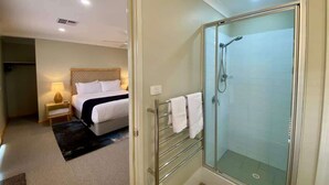 Une chambre d’hôtel comprenant un lit, une table de chevet, une lampe et une douche séparée par des parois en verre.