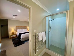 A hotel room with a bed, bedside table, lamp, and a glass-enclosed shower area.
