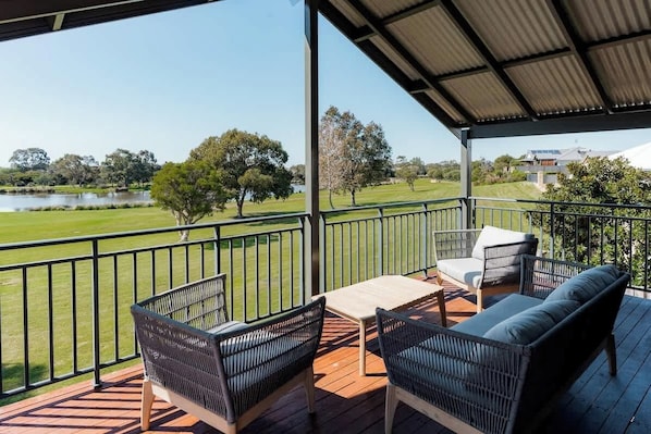 Eine überdachte Terrasse im Freien mit Rattanmöbeln und Blick auf einen See und einen Park.