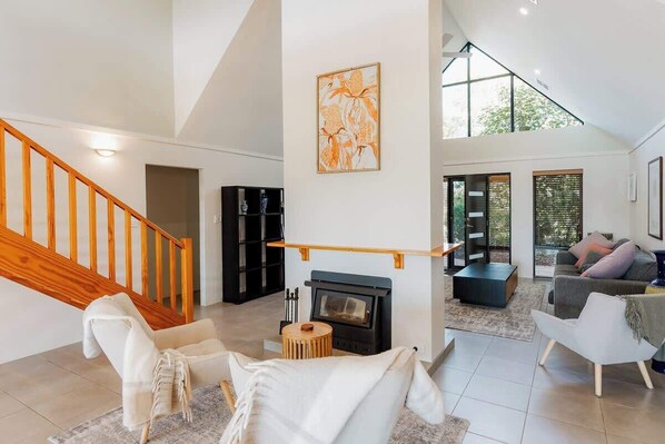 A spacious living area with a fireplace, a staircase, and a large window.