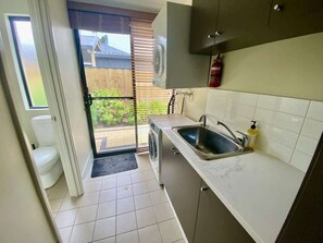 Eine kompakte Küche mit Spüle, Waschmaschine und einer Tür zu einem Balkon mit Gartenblick.