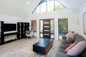 Ein modernes Wohnzimmer mit Flachbildfernseher, einer Couch, einem Couchtisch und einem großen Fenster.