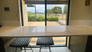 Une cuisine dotée d’un grand plan de travail, de deux tabourets et d’une vue sur un jardin, accessible par une porte vitrée.