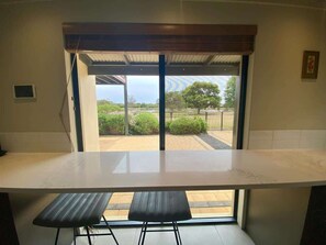 A kitchen with a large countertop, two stools, and a view of a garden through a glass door.