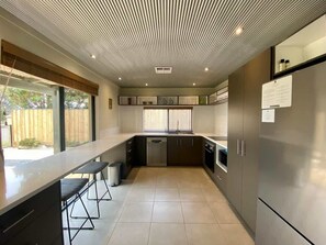 A modern kitchen with a long countertop, bar stools, a dishwasher, and a refrigerator.