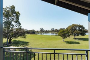 A view from a balcony overlooking a grassy area with trees and a body of water.