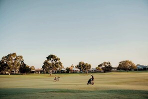 Un parcours de golf avec de vastes espaces couverts d’herbe, des arbres et des bâtiments situés au loin.