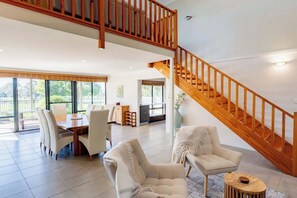 Un vaste espace de vie agrémenté d’un escalier en bois, d’une table à manger avec des chaises et d’une grande fenêtre.