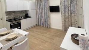 Une cuisine moderne avec des armoires blanches, un four encastré et un coin repas comprenant une table et des chaises blanches.