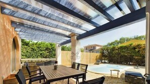 Une terrasse extérieure avec une table et des chaises, une piscine et un espace abrité offrant une vue sur le paysage environnant.