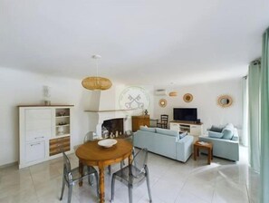 A modern living room with a dining table, sofa, TV, and decorative wall art.