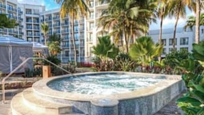 A hot tub surrounded by palm trees and a building with multiple balconies. - Studio Suite, Ocean View, at Margaritaville Rio Mar Resort, Puerto Rico! (Río Grande)