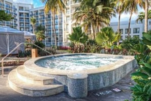 A hot tub surrounded by palm trees and a building with multiple balconies.