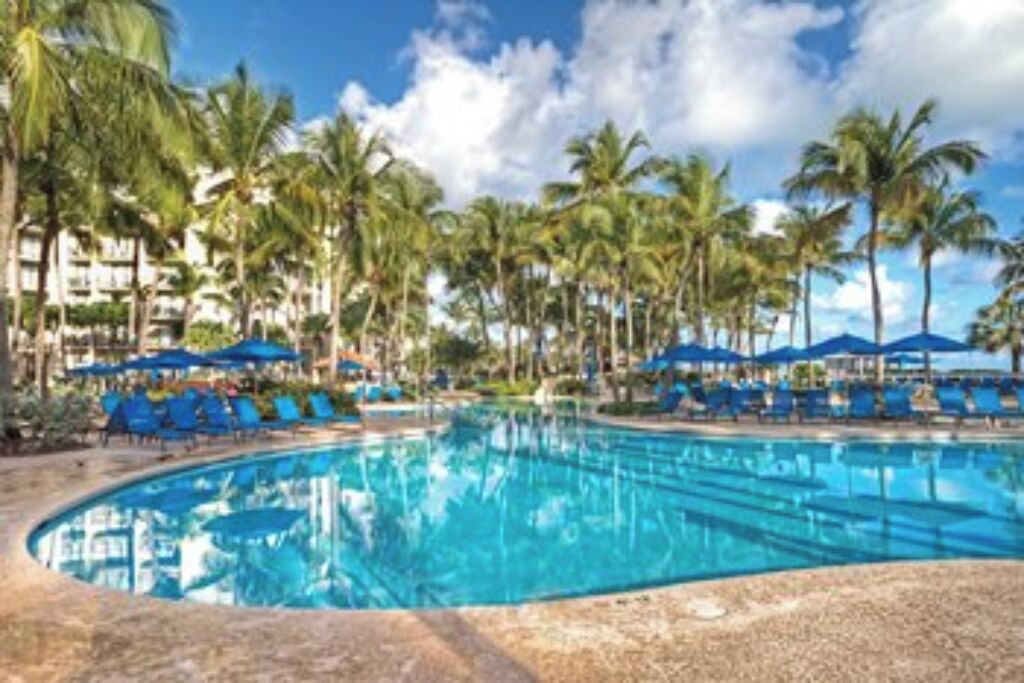 A swimming pool surrounded by palm trees and blue umbrellas.